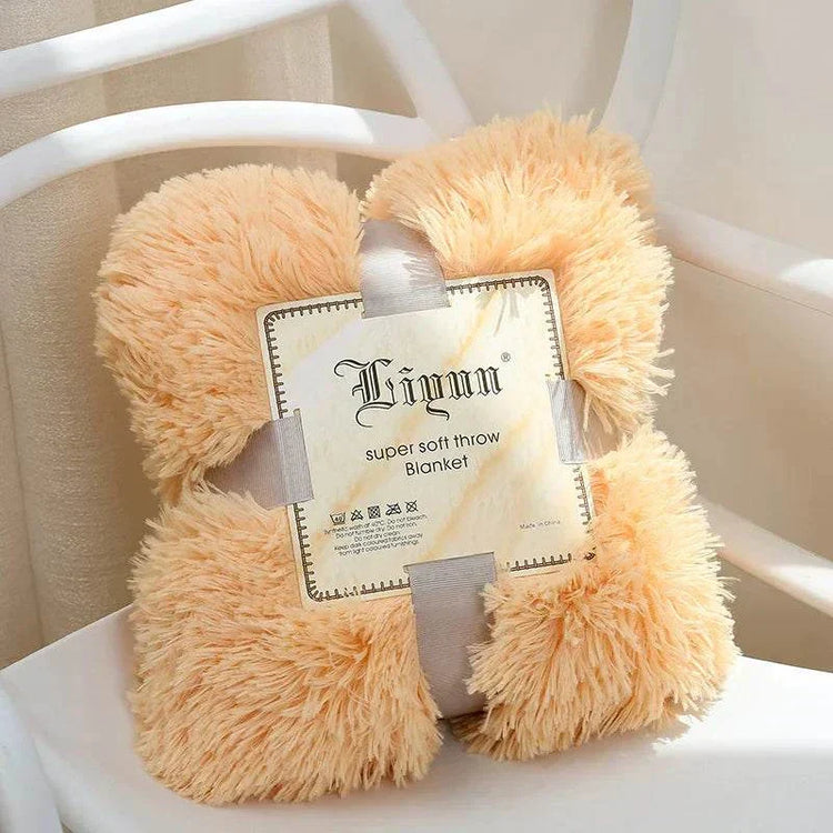 Soft fluffy coral fleece blanket in light peach color folded with label on white chair