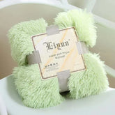 Light green super soft coral fleece blanket with fluffy texture, folded and secured with a gray ribbon on a white chair