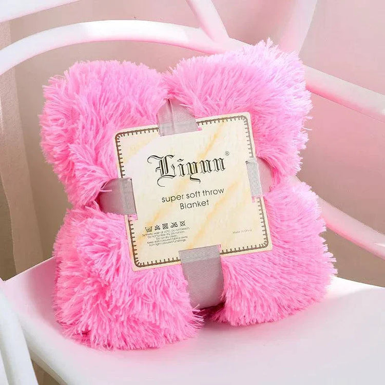 Pink super soft coral fleece blanket folded and strapped on a white chair
