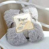 Fluffy gray coral fleece blanket folded with packaging label on white chair