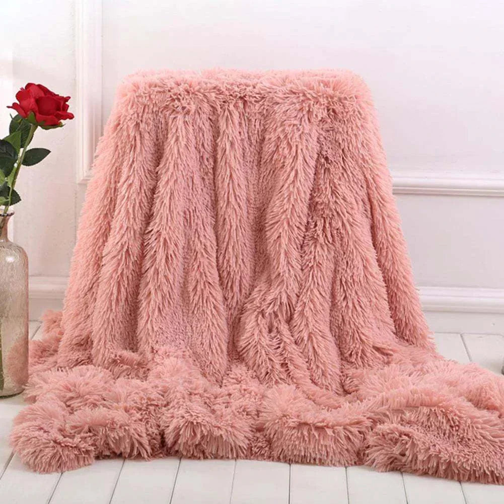 soft pink coral fleece blanket draped on floor beside red rose in vase