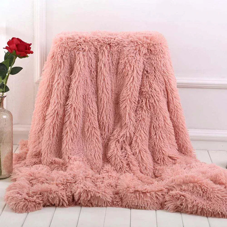 soft pink coral fleece blanket draped on floor beside red rose in vase