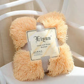 Plush peach coral fleece blanket folded with label on white chair, soft and cozy throw for sofa or travel